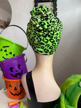 Load image into Gallery viewer, Green leopard print headscarf on a mannequin with Halloween-themed buckets in the background.
