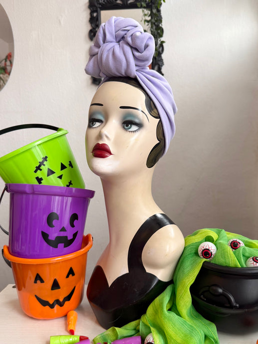 Mannequin head wearing lilac turban with Halloween-themed decorations 