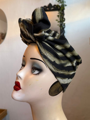 Mannequin head wearing a black and gray striped headscarf with a blurred background