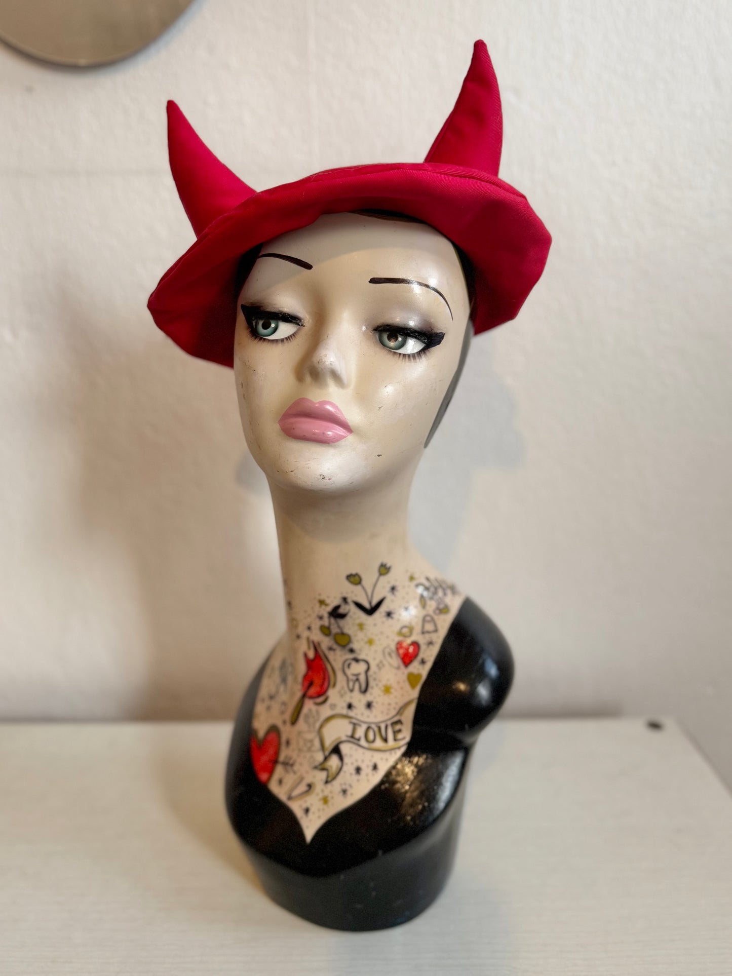 Female mannequin head with decorative tattoos wearing a horned beret hat on a plain background