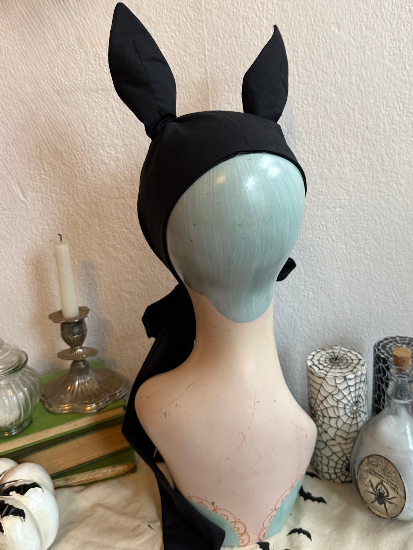 Mannequin head wearing a black gothic bat headband on a decorative background.
