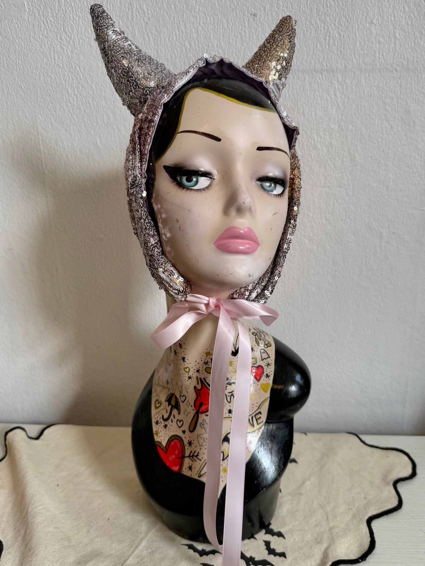 Mannequin head with decorative headpiece and pink ribbon on a plain background