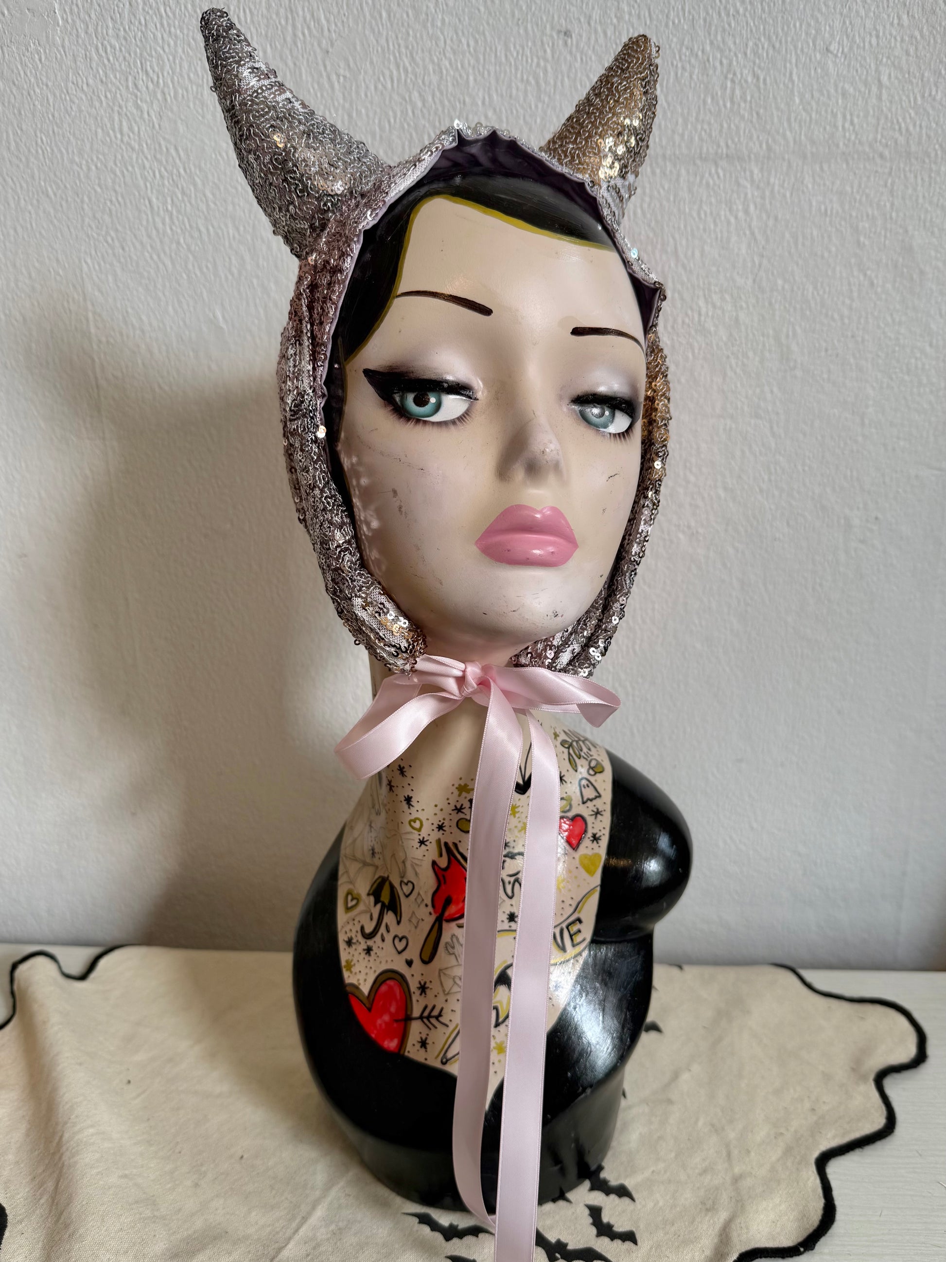 Mannequin head with decorative headpiece and pink ribbon on a plain background