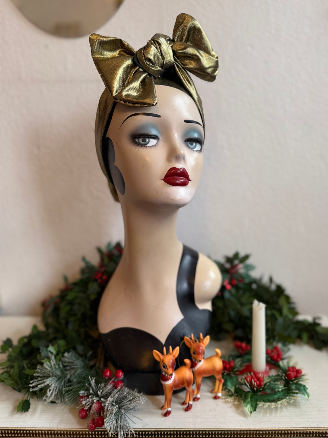 Mannequin head with gold headscarf, Christmas decorations, and deer figurines in background