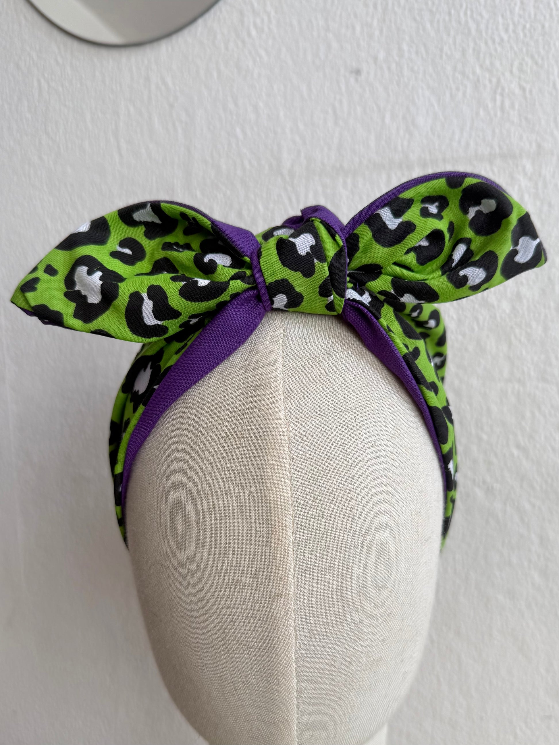 Green leopard print headband with purple bow on a mannequin head against a white background