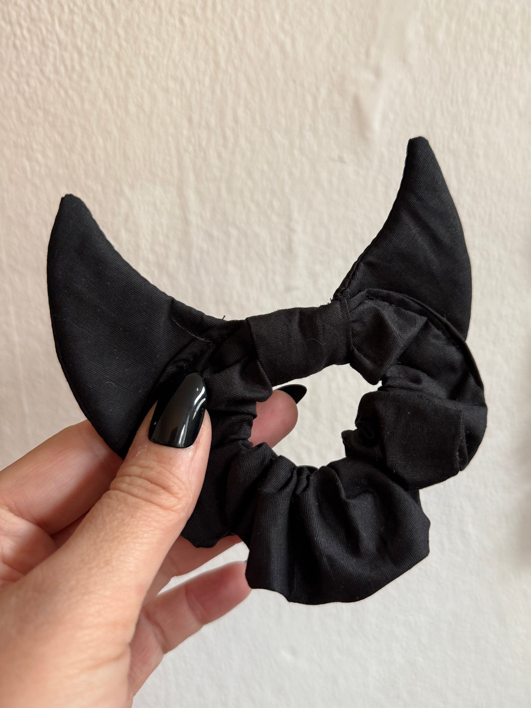 Black scrunchie with devil horns held by a hand against a neutral background
