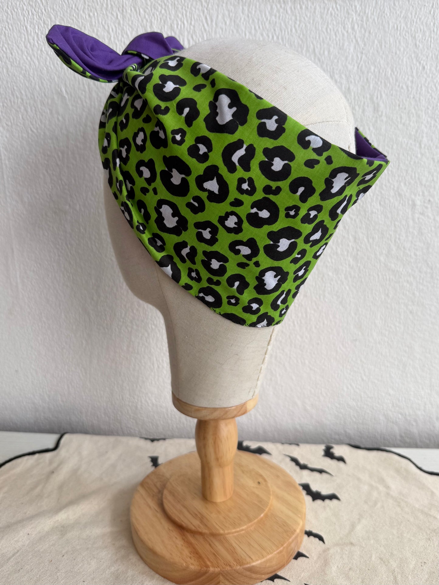 Green leopard print headscarf with purple accents on a mannequin head against a white background