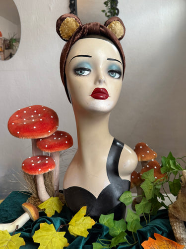 Mannequin head with bear ears surrounded by mushrooms and leaves
