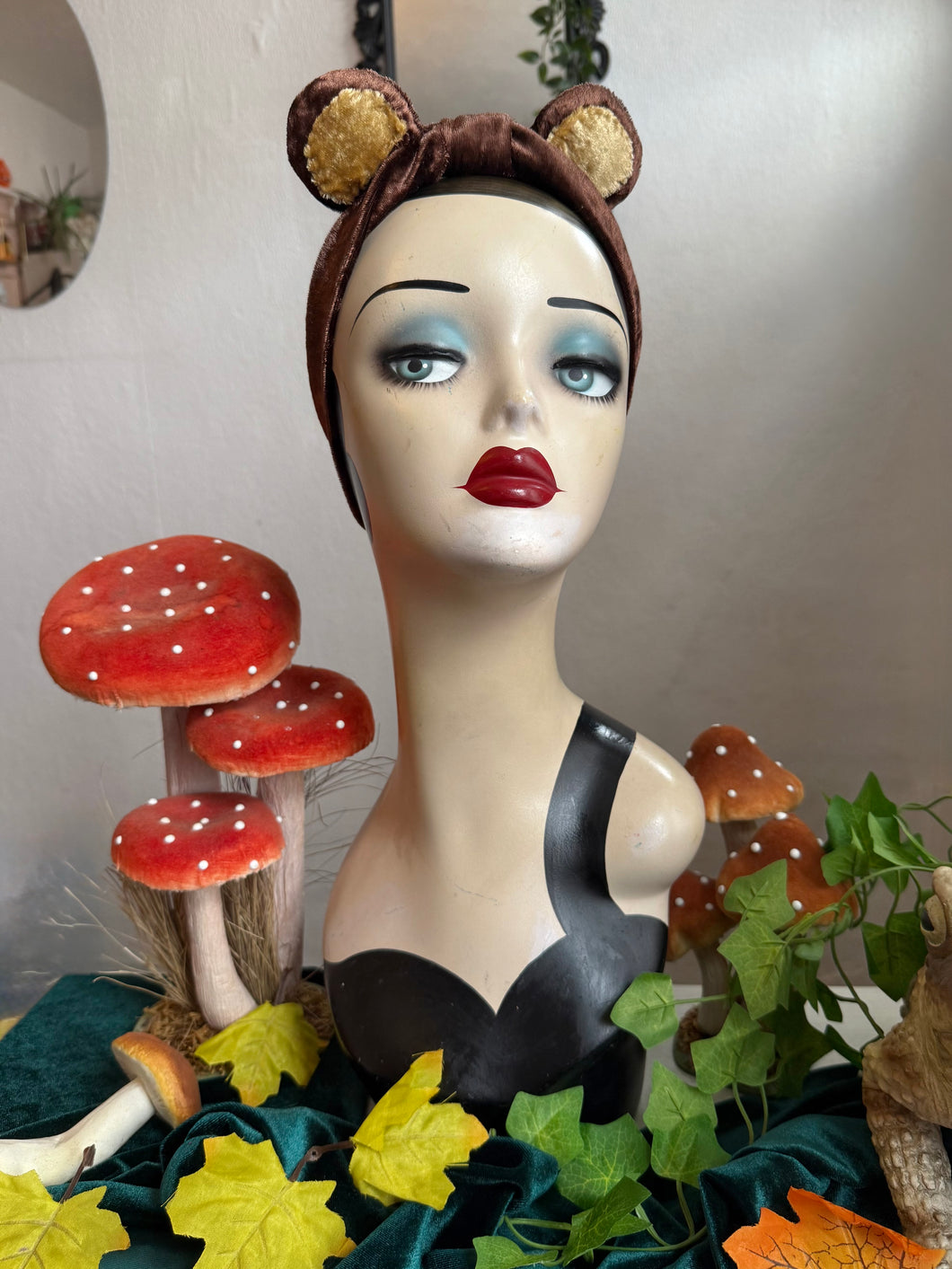 Mannequin head with bear ears surrounded by mushrooms and leaves