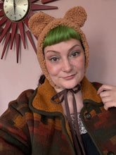 Load image into Gallery viewer, Person wearing a brown bear-themed hat with ears against a pink wall.