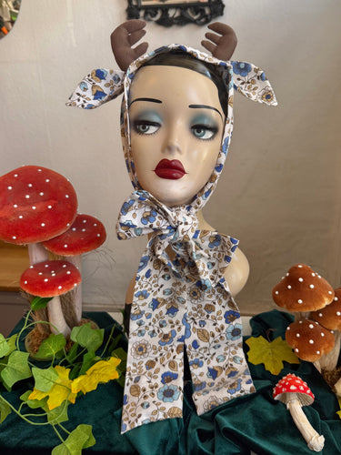 Display head with floral deer antler headband surrounded by decorative mushrooms and leaves.