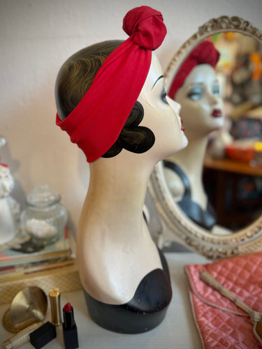 Mannequin head with red headband in front of a mirror on a table.