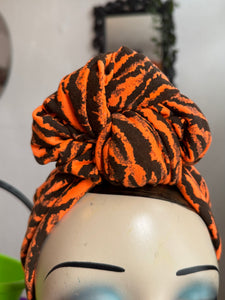 Orange and black tiger print patterned headscarf on a mannequin head against a neutral background