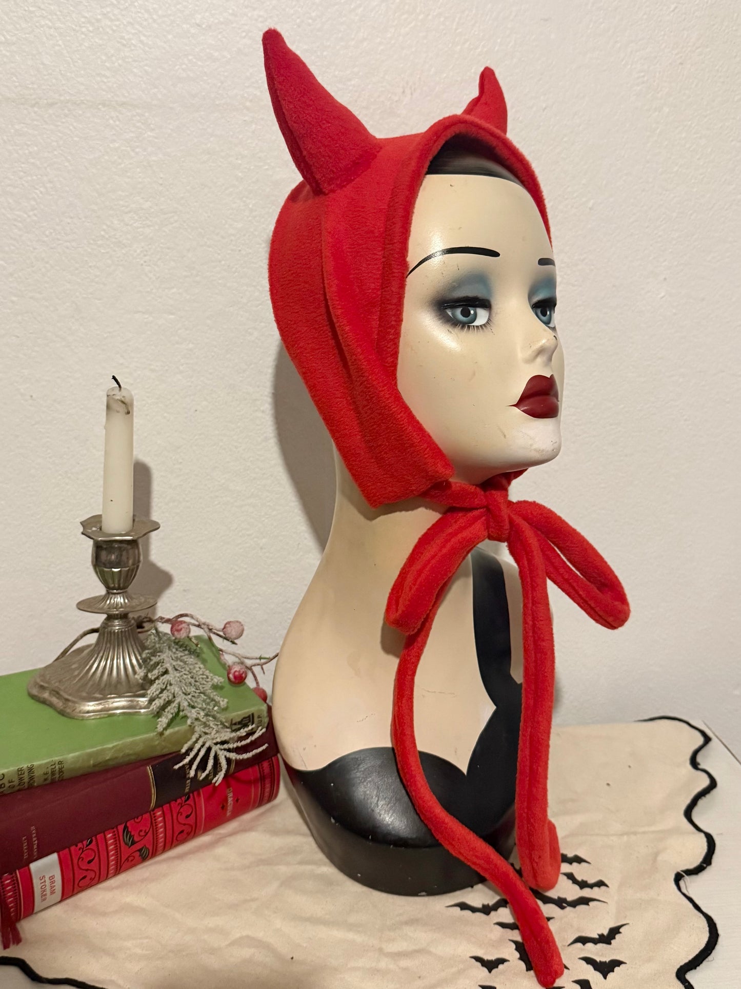 Mannequin head wearing a red devil horn headband with a candle and decorative items in the background.