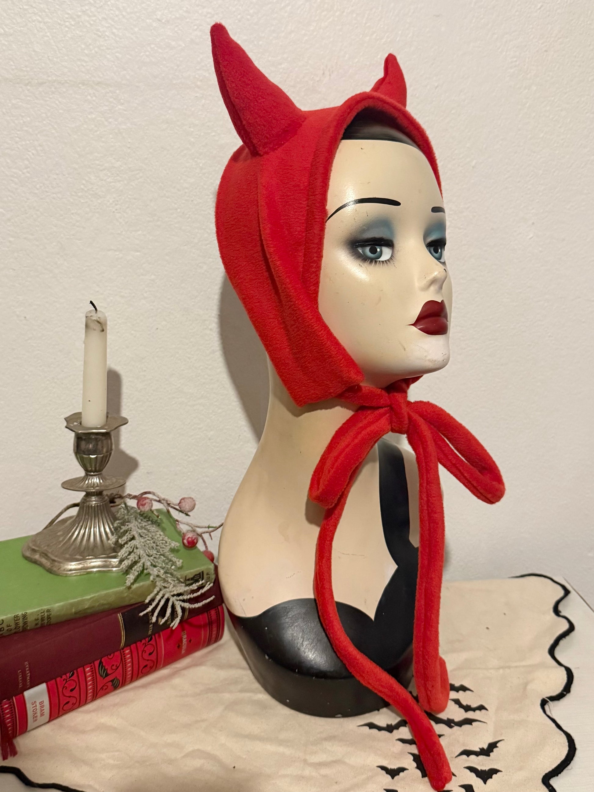 Mannequin head wearing a red devil horn headband with a candle and decorative items in the background.