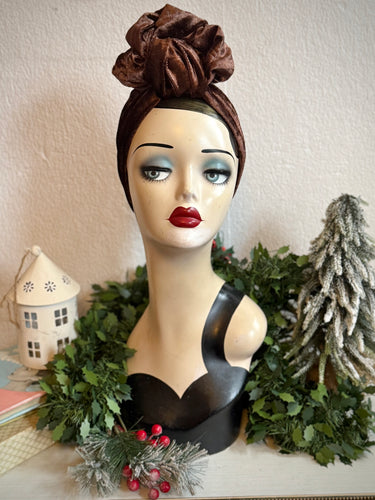 Mannequin head with a brown velvet headscarf and festive decorations on a white background