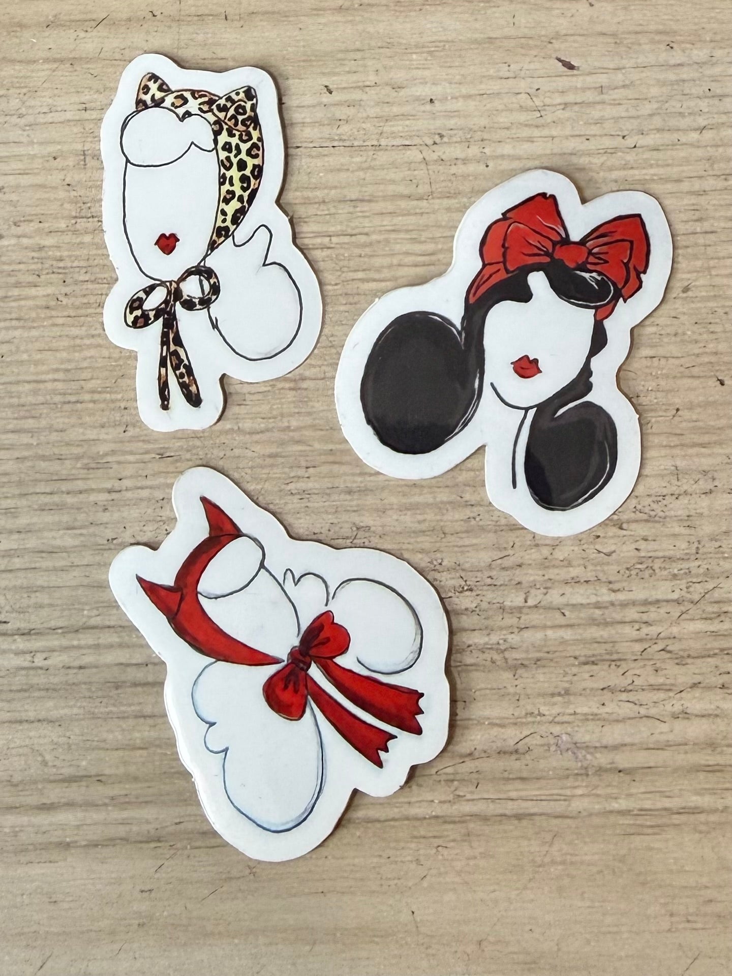 Three decorative stickers with cartoon faces wearing bows on a wooden surface