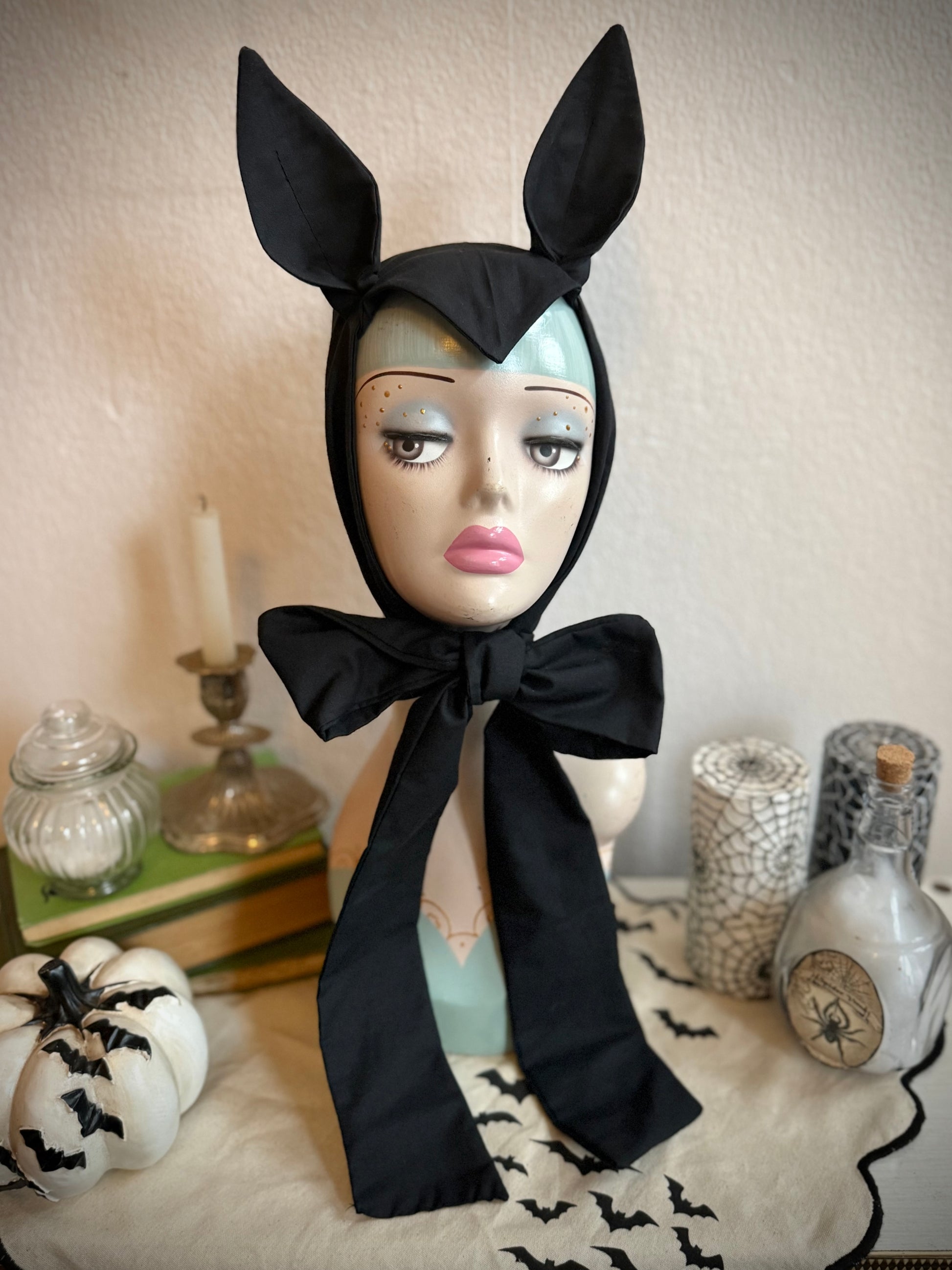 Mannequin head wearing a black gothic bat headband on a decorative background.