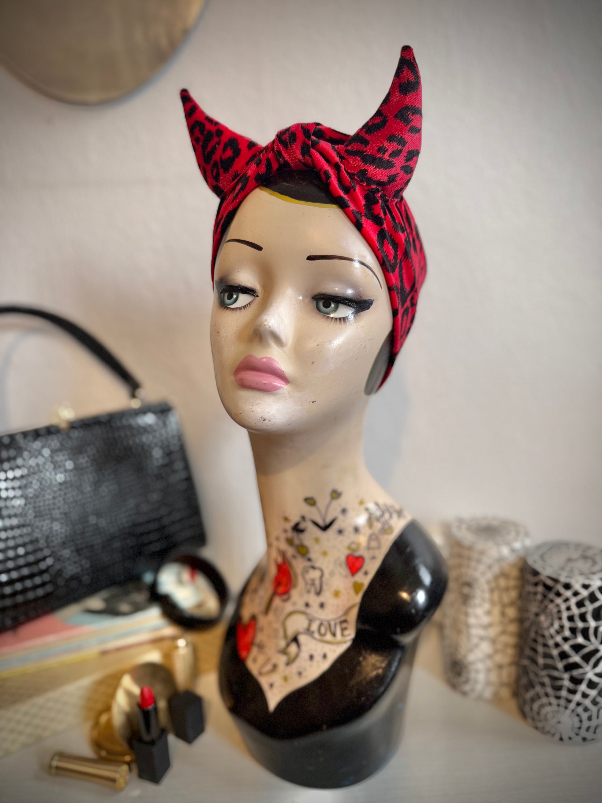Mannequin head with leopard print headband and tattoos, surrounded by makeup items.