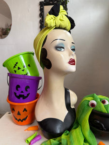 Mannequin head with Halloween-themed decorations including buckets and a green headband.