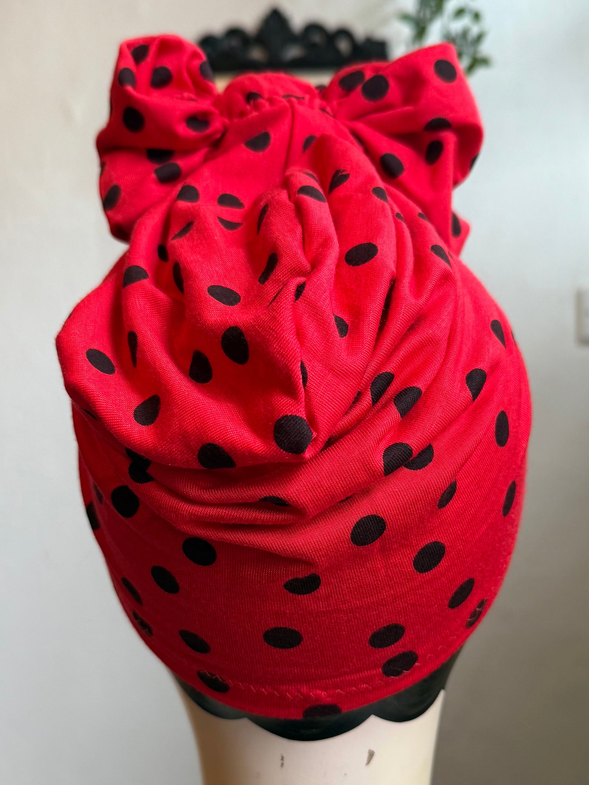 Mannequin head wearing a red polka dot turban with a neutral background