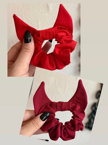 Red scrunchie with devil horns held by a hand against a neutral background