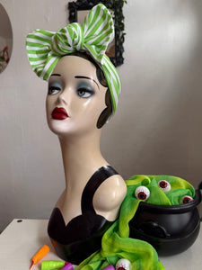 Mannequin head with green and white halloween striped headscarf, black top, and green scarf with eye decorations.