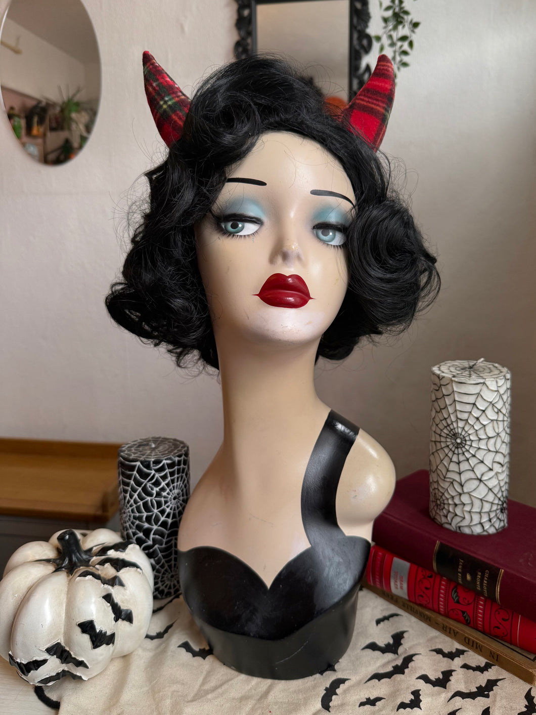 Mannequin head with black wig, red lipstick, and red devil horns against a neutral background.