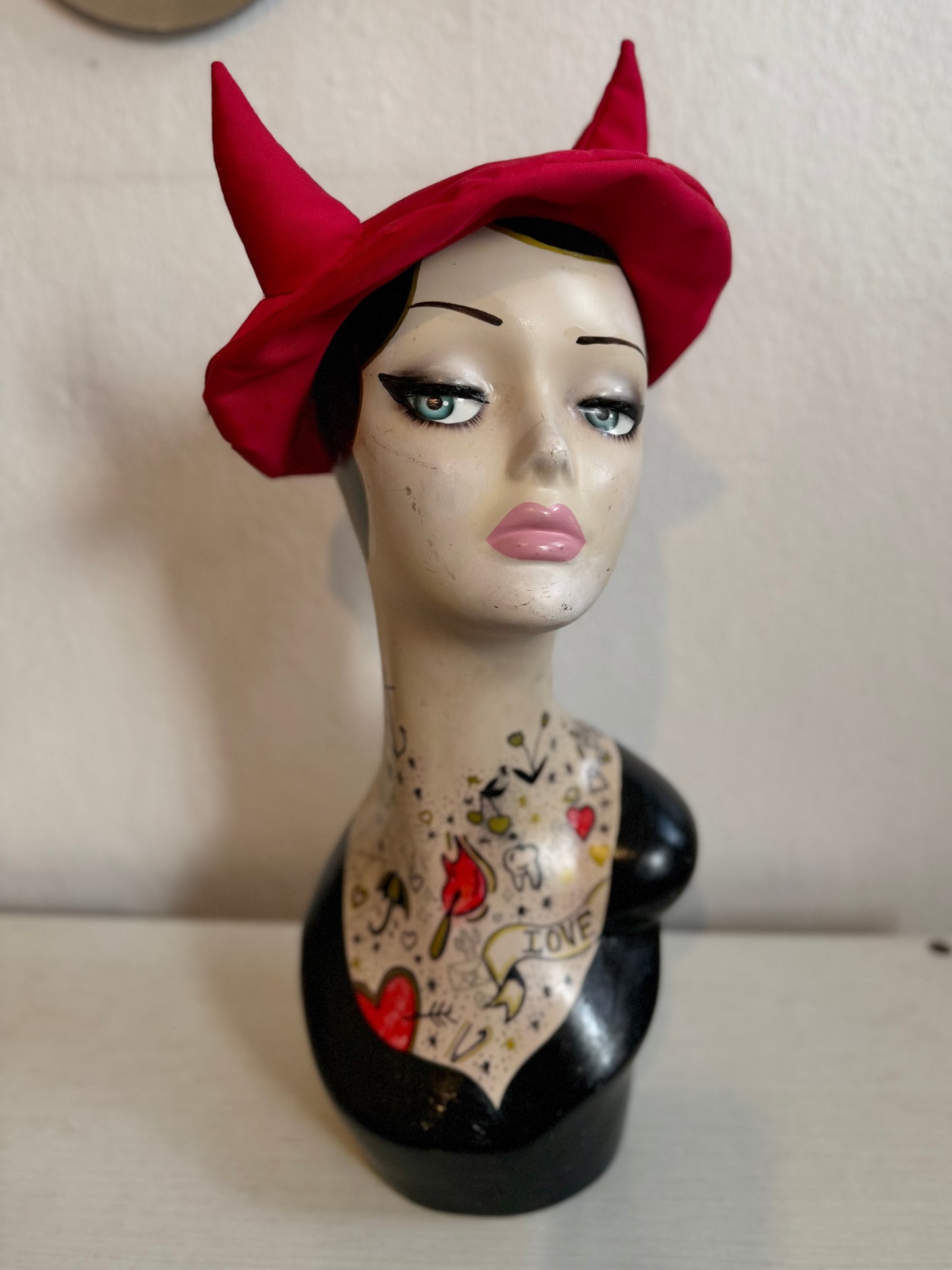 Female mannequin head with decorative tattoos wearing a horned beret hat on a plain background
