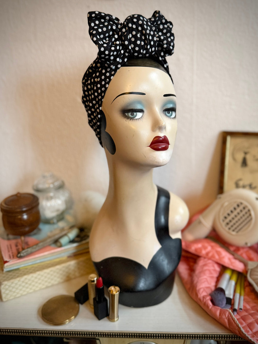 Mannequin head with polka dot headband and makeup items on a table
