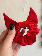 Load image into Gallery viewer, Red scrunchie with devil horns held by a hand against a neutral backgrounD