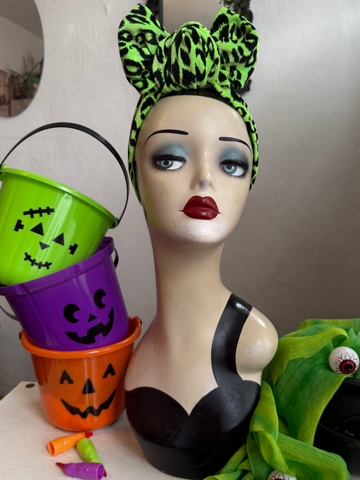 Mannequin head with green leopard print headband, Halloween buckets, and colorful accents.