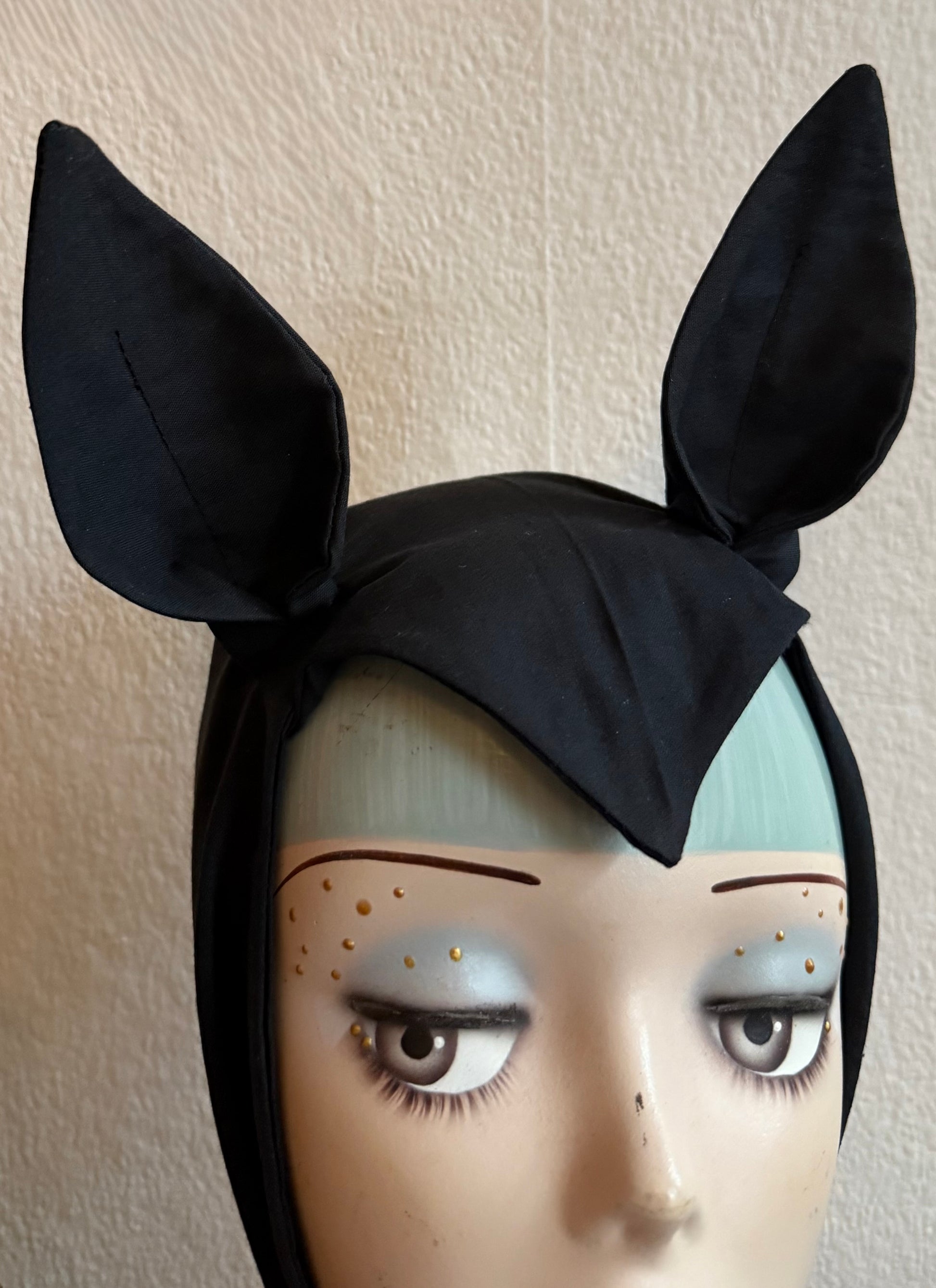 Mannequin head wearing a black gothic bat headband on a decorative background.
