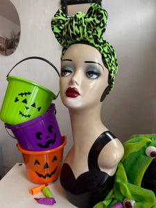 Mannequin head with Halloween-themed green headband and buckets on a white surface.