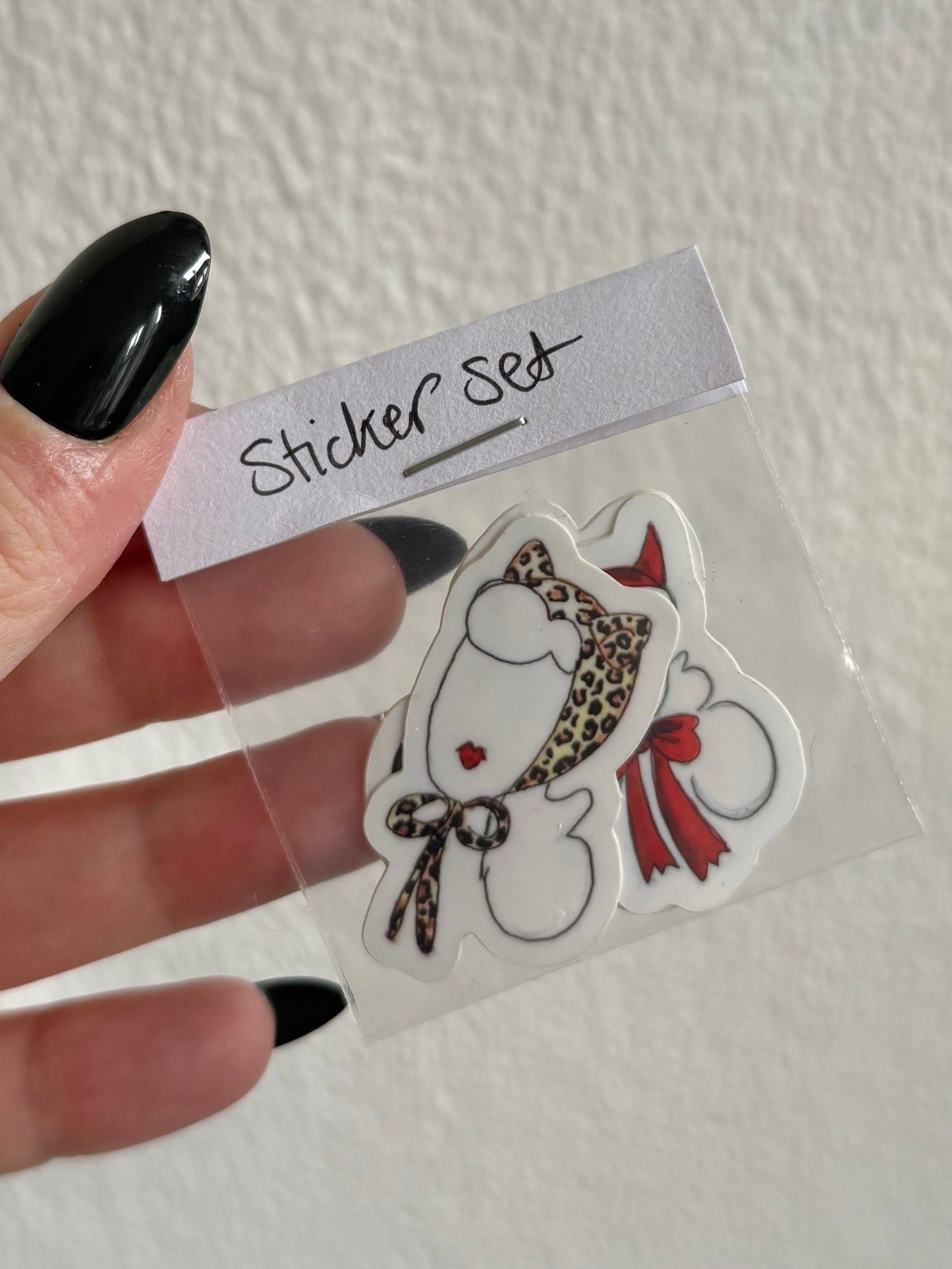 Hand holding a clear plastic bag with a sticker set featuring a cartoon character with a leopard print bow and red ribbon.