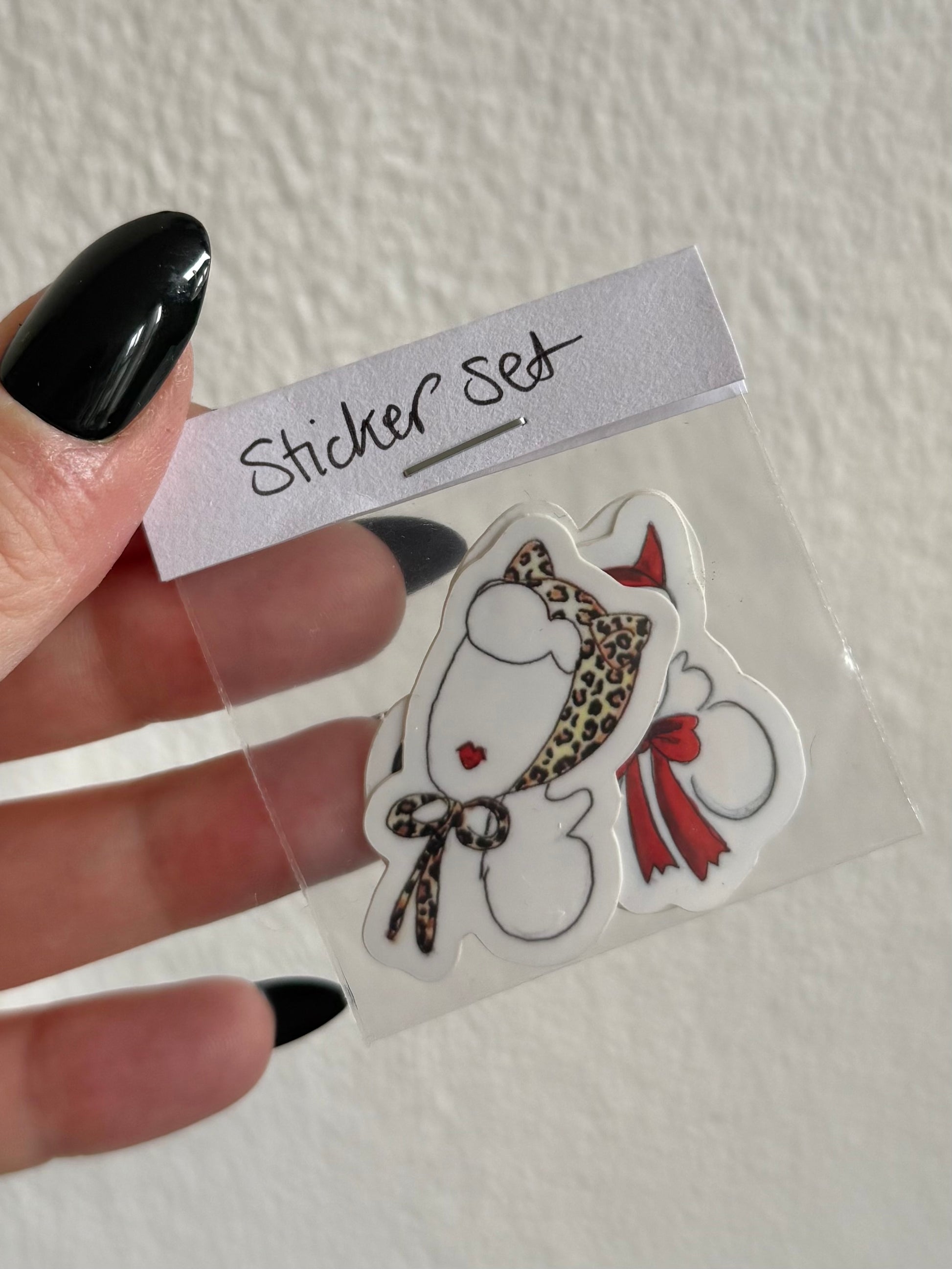 Hand holding a clear plastic bag with a sticker set featuring a cartoon character with a leopard print bow and red ribbon.