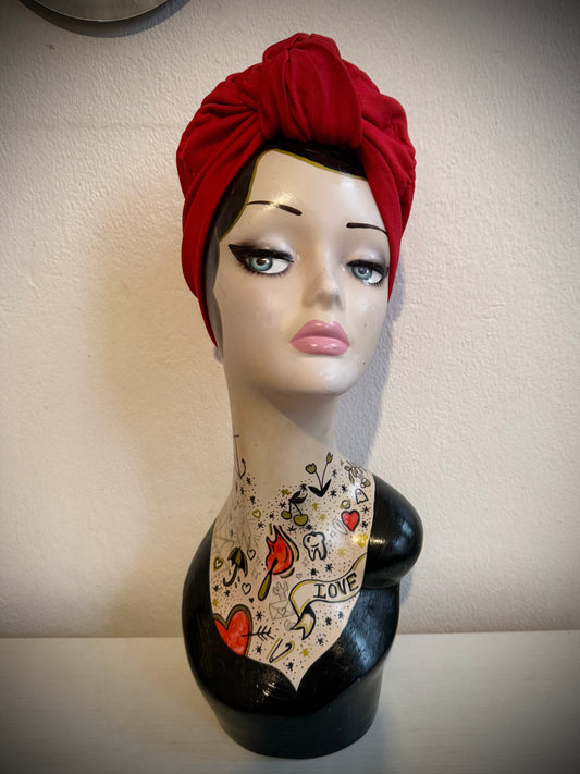 Mannequin head with a red turban with tattooed neck against a plain background