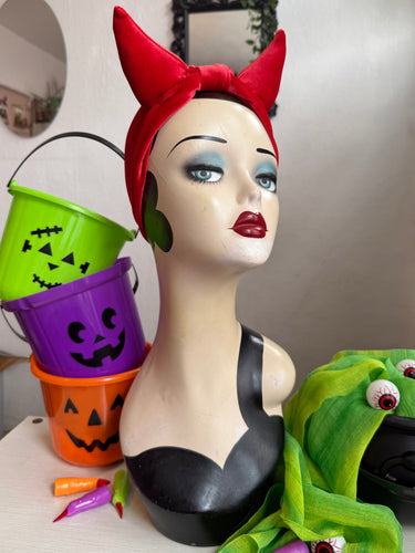 Mannequin head with Halloween-themed accessories including a red headband, colorful buckets, and green scarf.