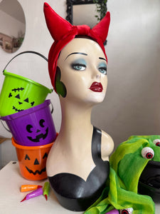 Mannequin head with Halloween-themed accessories including a red headband, colorful buckets, and green scarf.