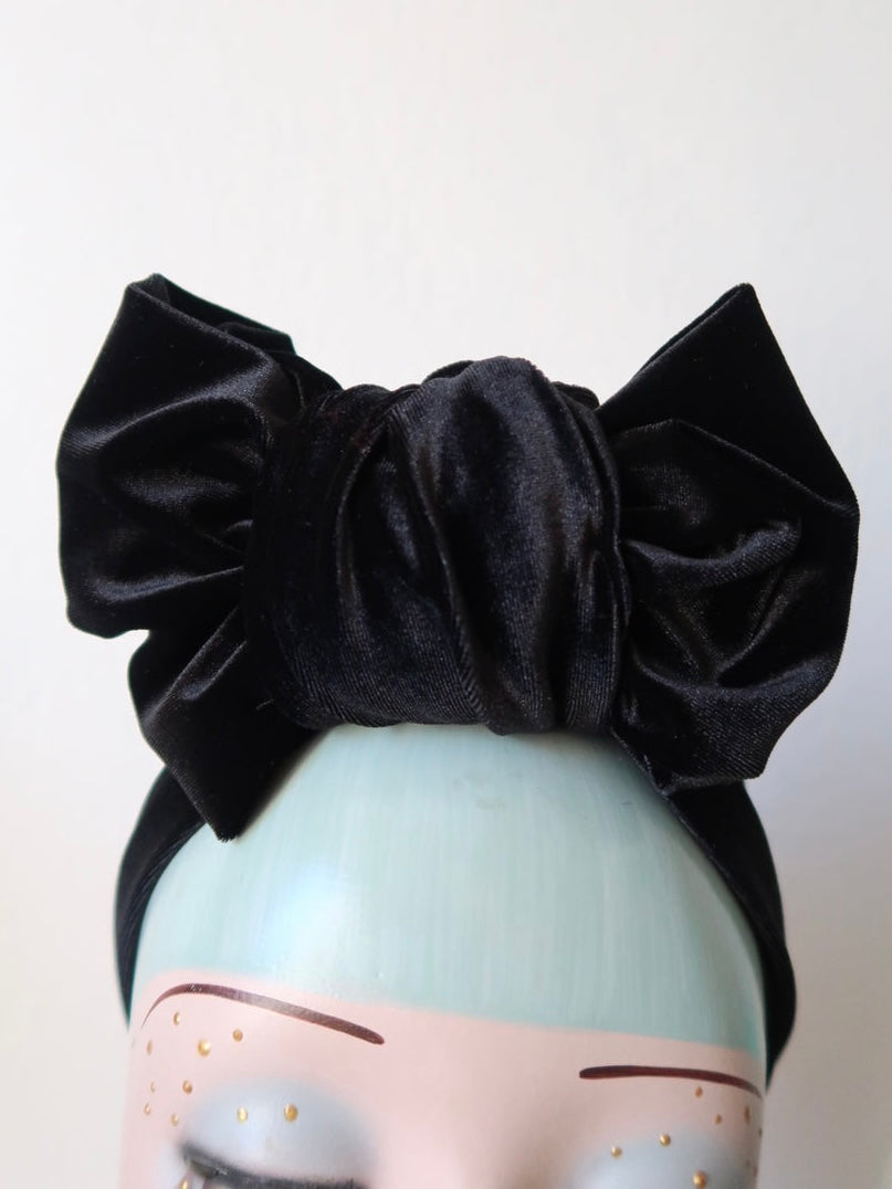 A black smooth velvet pre-tied turban or headband with a knot on a mannequin head.