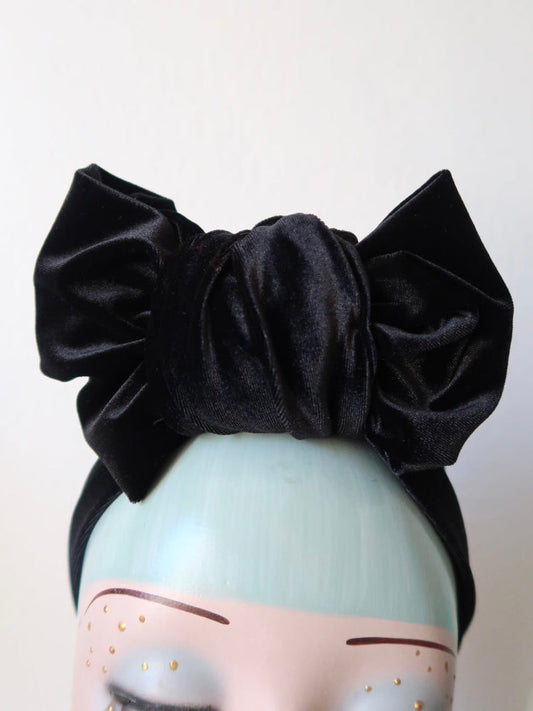 A black smooth velvet pre-tied turban or headband with a knot on a mannequin head.