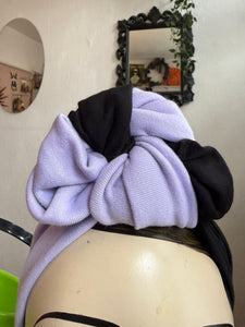 Mannequin head with a black and purple garment draped over it against a neutral wall.
