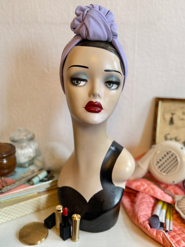Mannequin head with a purple headscarf and makeup items on a table.