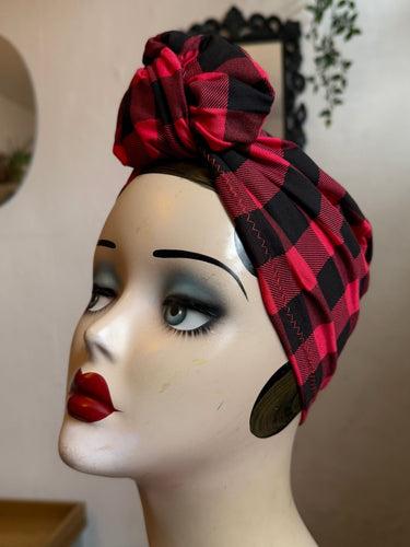 Mannequin head wearing a red buffalo check turban with a neutral background