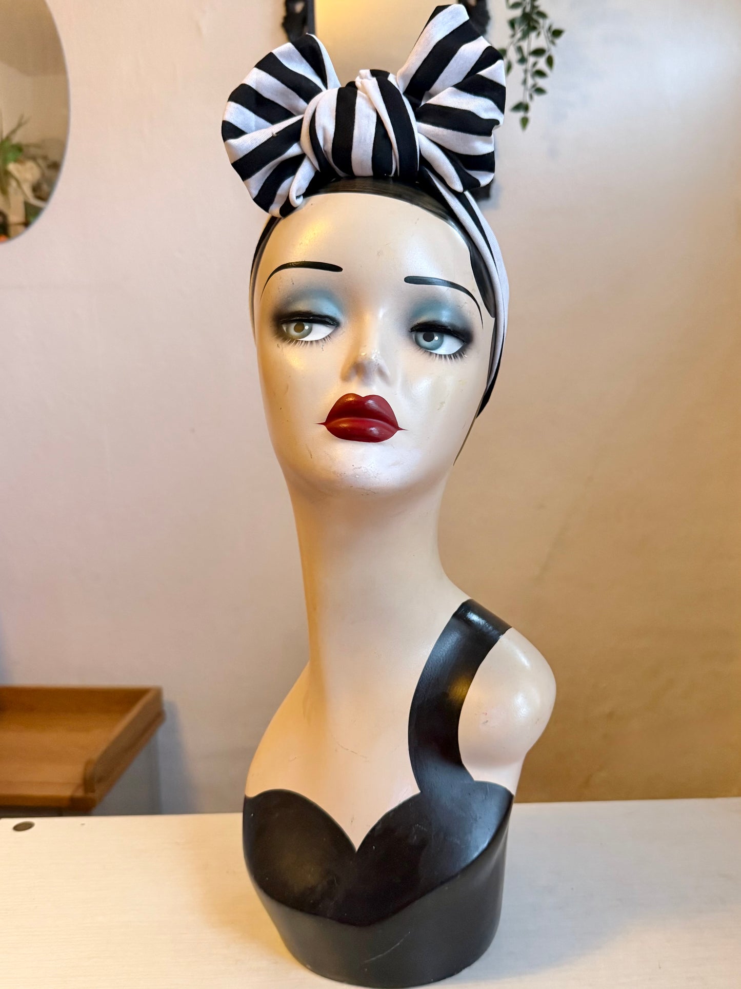 Mannequin head with black and white striped headband on a plain background