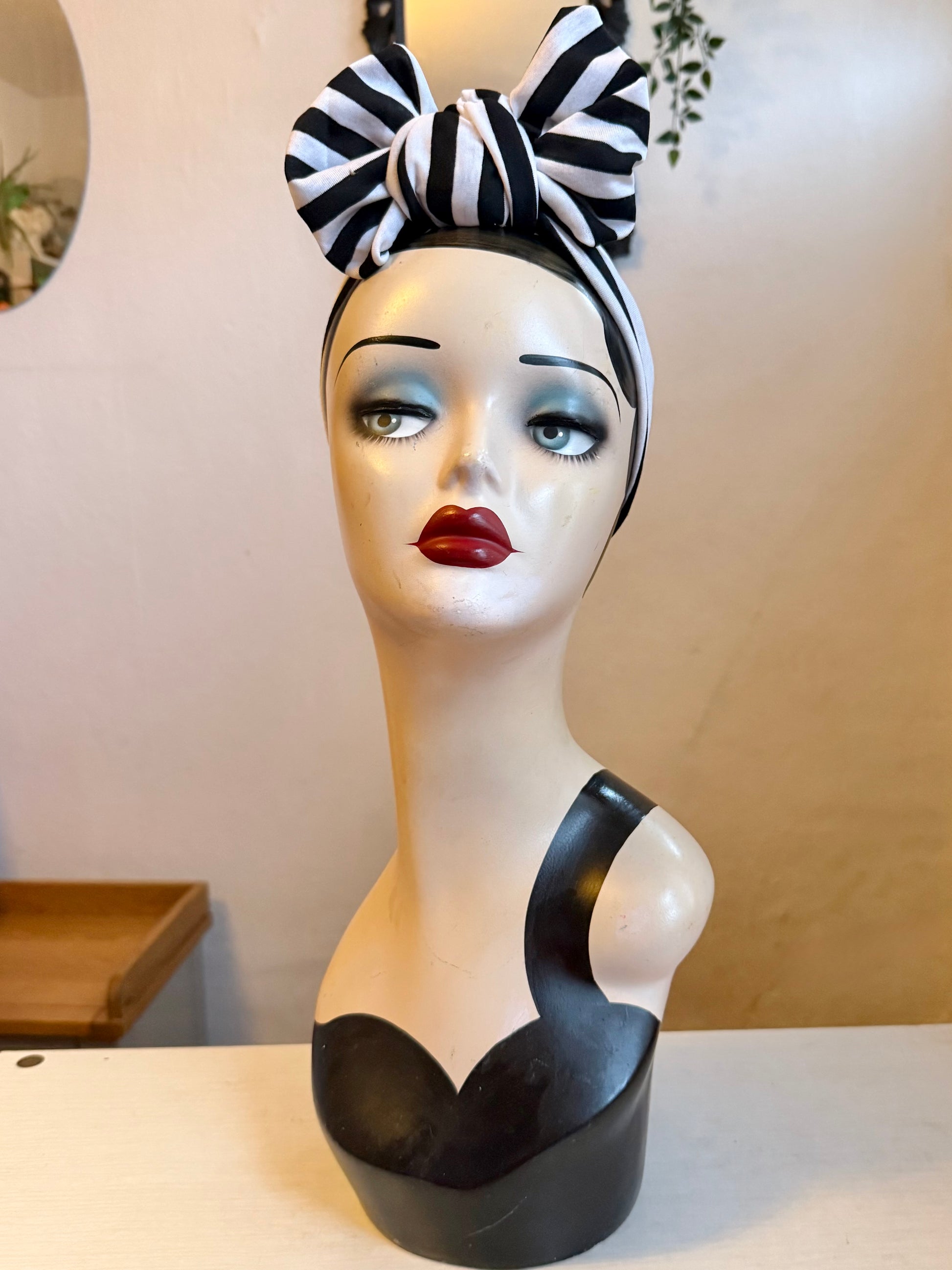 Mannequin head with black and white striped headband on a plain background