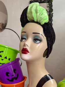 Mannequin head with Halloween makeup and green hair bow, next to colorful buckets.