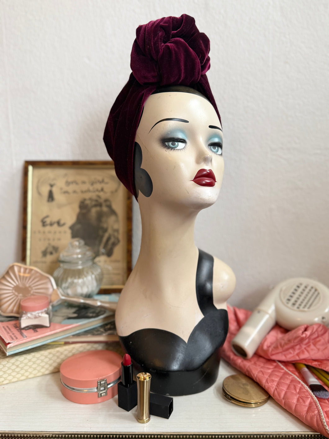 Display head showing a glamorous rich red velvet turban with a vintage dressing table backdrop