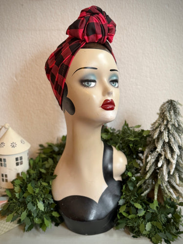 Mannequin head with a red and black plaid headscarf against a neutral background with Christmas decorative elements.