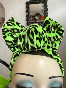 Neon green and black leopard print headband on a mannequin head with a mirror and decorative elements in the background.